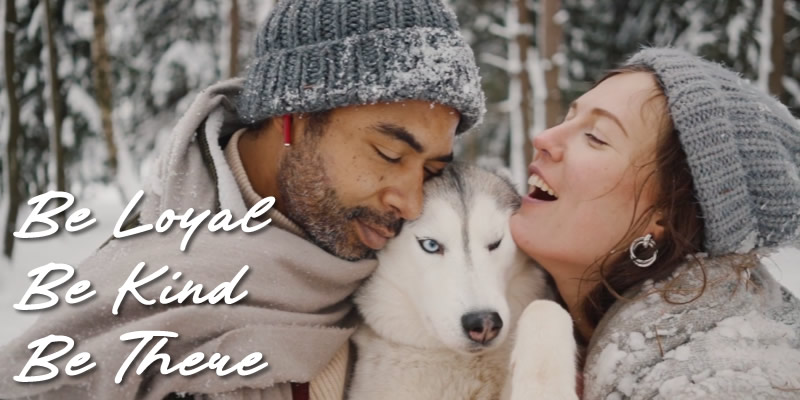 A man and woman in the snow, hugging their husky dog